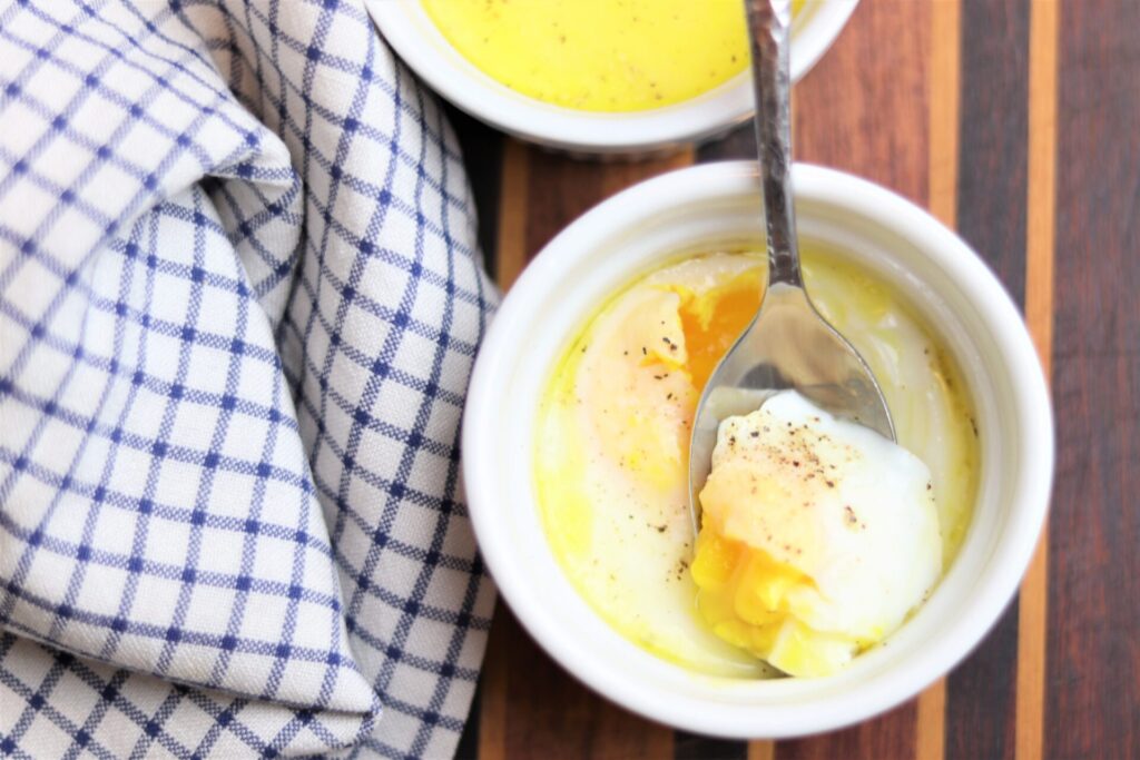 Cozy Butter Eggs, Egg cooked in a white ramekin with bright yellow yolk in a spoon