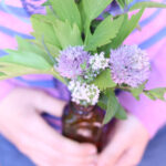 Ways to make spring come sooner, small brown bottle in child's hands containing herbs and chive blossoms